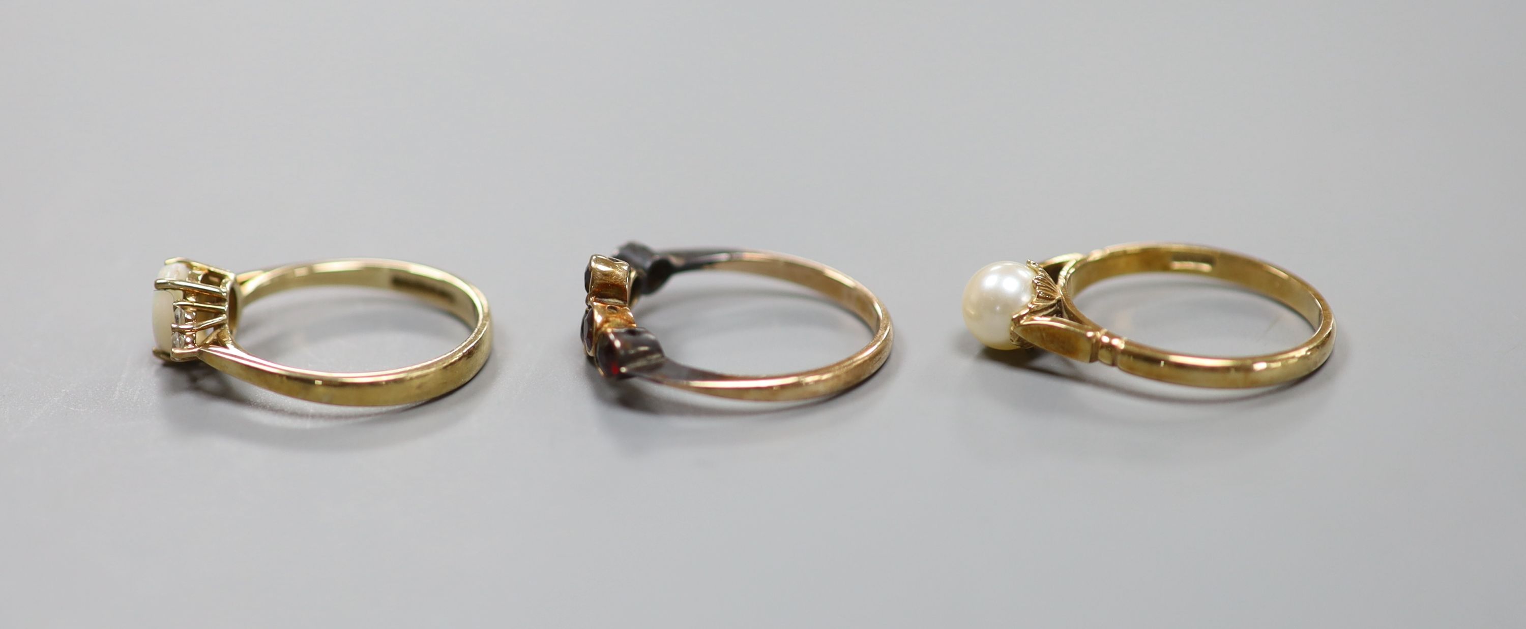 A 9ct yellow gold garnet-set ring, a similar cabochon opal and small diamond ring and a similar pearl-set ring (3) 6.5g